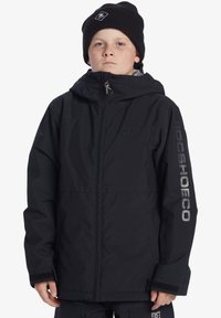 Svart huva jacka tillverkad av texturerat tyg, med dragkedja fram, elastiska ärmar och logografik på ärmen och bröstet.