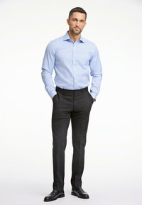 Camicia azzurro chiaro con motivo sottile, maniche lunghe e polsini abbottonati, abbinata a pantaloni neri su misura e scarpe nere.