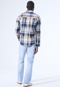 Langarm geruite shirt in blauw, crème en oranje tinten. Heeft knopenmanchetten en een rechte snit. Gekocht met lichtgekleurde jeans en schoenen.