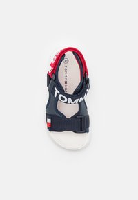 Siniset ja punaiset lasten sandaalit, joissa on säädettävät hihnat, valkoinen pohja ja erottuva "TOMMY HILFIGER" -brändäys ylähihnassa. Koko 31.