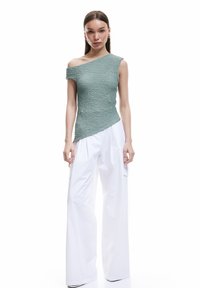 Top verde, texturizado y asimétrico con un solo hombro y un cuerpo ajustado, combinado con pantalones anchos blancos.