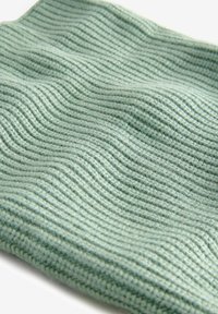 Strickstoff in Hellgrün, mit einem strukturierten, wellenförmigen Muster. Das Material wirkt weich und flexibel mit sichtbaren Nähdetails.