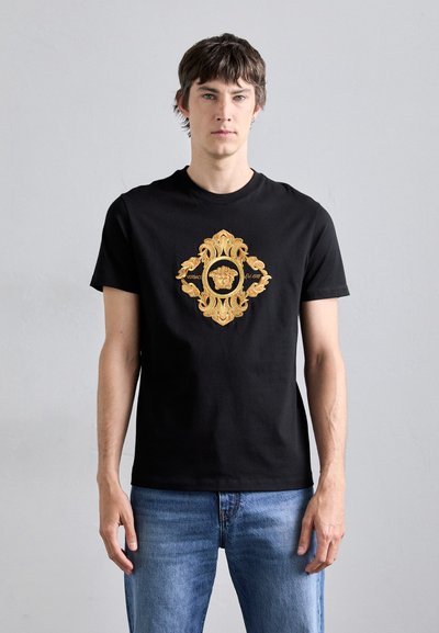 Czarny bawełniany t-shirt z centralnym, złotym haftowanym wzorem przedstawiającym ozdobne wzory z motywem lwa.