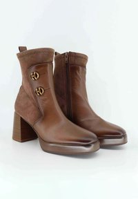 Stivaletti brown con corpo in pelle liscia, dettagli in suede, due bottoni in metallo dorato e tacco a blocco testurizzato. Chiusura con zip laterale.