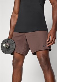 Brown Nike athletic shorts with a textured fabric, paired with a black fitted top, held with a black weight in one hand.