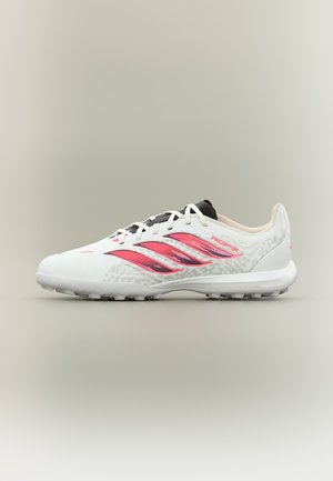 Biało-różony but piłkarski Adidas Predator z czarnym językiem i teksturowaną podeszwą przeznaczony do gry na sztucznej murawie, widok z boku na neutralnym tle.