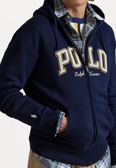 Tumesinine tõmblukkidega kapuutsiga sviiter, millel on broderi "POLO" logo ja "Ralph Lauren" tekst; omadused on kapuutsi string, ning sooniku varrukad. Kombineeritud ruudulise särgiga.