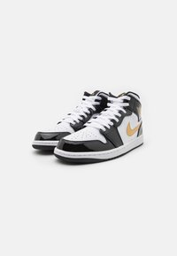 Vysoké tenisky s bílou koženou základnou, černými lakovanými akcenty a zlatým logem Nike, kulatou špičkou a bílými tkaničkami.