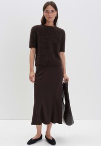 Pull court en mélange de mohair marron foncé à manches courtes, jupe midi marron ajustée avec un ourlet festonné, et ballerines noires, accessoirisées avec un sac noir.