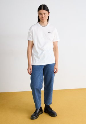 Hvid bomulds t-shirt med korte ærmer og et sort Puma-logo, parret med løse blå denim jeans og sorte snørresko.