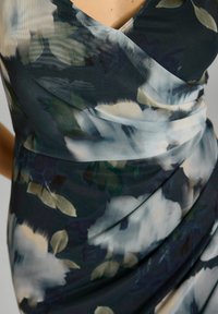 Kleid aus transparenter, floral gemusterter Stoff mit dunklen Grüntönen und Marineblau, ausgestattet mit Falten-Details und einem V-Ausschnitt.