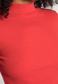 Camisola de gola alta vermelha com textura em canelado. A vista em close destaca os detalhes intricados do tecido.