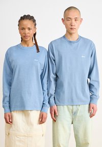 Light blue long-sleeve shirts featuring a small "obey" logo in white. The fabric appears soft, with a casual fit and ribbed cuffs.
