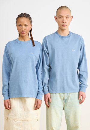 Chemises à manches longues bleu clair présentant un petit logo "obey" en blanc. Le tissu semble doux, avec une coupe décontractée et des poignets côtelés.