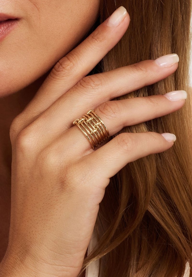Gouden multi-band ring met in elkaar grijpende ontwerpen, een gladde textuur en een gepolijste afwerking, gedragen aan een hand met natuurlijke nagels.