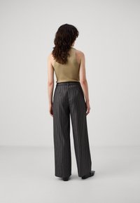 Jasnooliwkowy top na ramiączkach oraz czarne, szerokie spodnie z wysokim stanem w pionowe białe paski. Gładka tekstura, minimalistyczny design, zestawione z czarnymi butami.