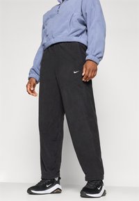 Czarne polarowe spodnie dresowe o luźnym kroju, z bocznymi kieszeniami i białym logo Nike. Połączone z jasnoniebieską bluzą i czarnymi tenisówkami.