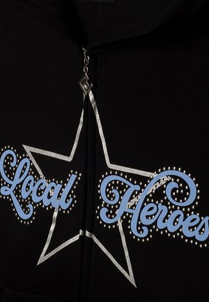 Czarna bluza z kapturem na zamek z napisem "Local Heroes" w niebieskim, stylizowanym kroju, obramowanym srebrem i ozdobionym dżetami, z graficznym wzorem gwiazdy.