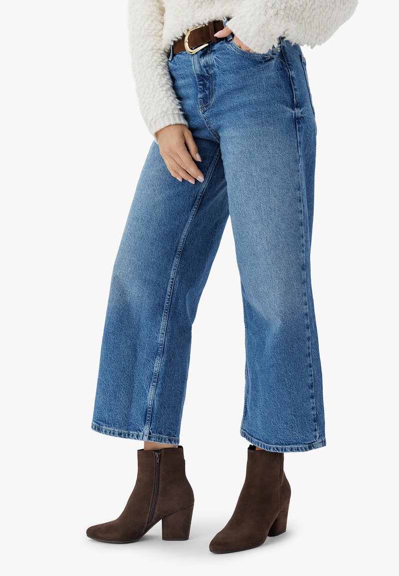 Jeans de tiro alto en tonos azul claro con pierna ancha y detalles desgastados, combinados con botines de ante marrón con tacón de bloque.