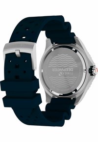 Montre Timex avec un boîtier en acier inoxydable, un bracelet en silicone noir perforé, un fond argenté à motif ondulé et une couronne classique.