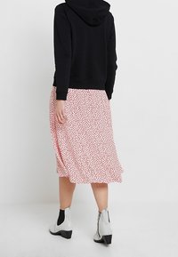 Felpa nera con cappuccio abbinata a una gonna a fantasia floreale rosa. La gonna ha un taglio di lunghezza media e una silhouette fluida, indossata con stivali alla caviglia.