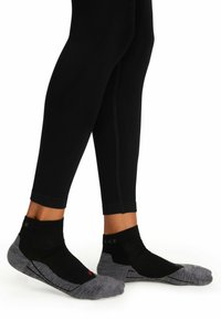 Schwarze Sportstrümpfe mit grauen Akzenten, mit einem niedrigen Schnitt und strukturiertem Material. Sichtbares Branding an der Oberseite und Designlinien entlang der Seiten.