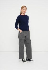 Pulover tricotat bleumarin cu guler roșu, asortat cu pantaloni cargo gri, cu multiple buzunare și o croială lejeră, purtați cu adidași negri cu glezna înaltă.