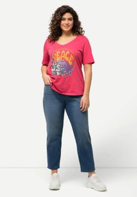 Vaaleanpunainen V-pääkohdan t-paita, jossa on "RAUHA" -grafiikka ja kukkakuosi, yhdistettyinä sinisiin farkkuihin. Valkoiset tennarit täydentävät asua.