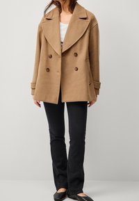 Kamelkleurige dubbelgebreide jas met een brede revers, voorzien van bruine knopen, zijzakken en een zachte, gestructureerde stof.