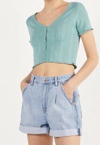 Ljusblå ribbad kortad tröja med V-ringning och knappstängning, kombinerad med högmidjade jeansshorts med uppvikta mudd i en urtvättad look.