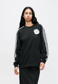 Μαύρο φούτερ με λευκές ρίγες στα μανίκια, με υφασμένη, κυκλική στάμπα στο στήθος. Απαλό ύφασμα, άνετη εφαρμογή.