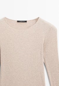 Maglietta a maniche lunghe beige a costine con scollo rotondo. Realizzata in tessuto morbido, presenta una texture sottile e un design aderente. Etichetta del marchio visibile.