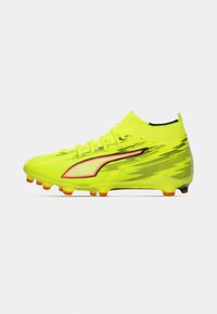 Zapatilla de fútbol de color amarillo brillante con ajuste ceñido, parte superior texturizada, acentos en negro y rojo, y suela exterior con tacos naranjas para tracción.