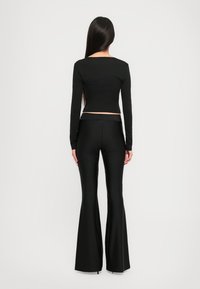 Black long-sleeve crop top paired with flared black pants, both in a smooth, fitted material. Back view shows minimal detailing and clean lines.