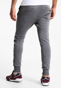 Szare dresy z elastycznymi mankietami i tylnymi kieszeniami, wykonane z miękkiego materiału. Nosi się je z bordo i białymi trampkami New Balance.