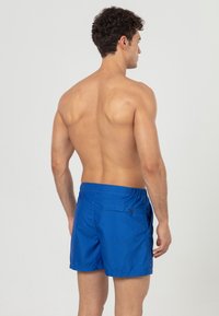 Blauwe zwembroek met een gestructureerd patroon en een elastische tailleband, met een achterzak. De stof lijkt lichtgewicht en sneldrogend.