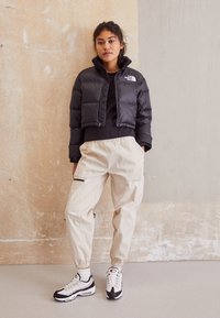 Jachetă cropped, căptușită, neagră, cu guler înalt, pantaloni cargo bej cu talie elastică și adidași negru-albi cu accente roșii.