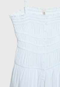 Vestido blanco sin tirantes con textura fruncida, botonadura frontal y diseño en capas. Tejido ligero con detalles fruncidos y una silueta fluida.