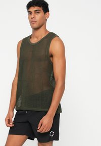 Olive green tank top made of mesh fabric, featuring a scoop neck and sleeveless design. Paired with black shorts; logo printed on shorts.