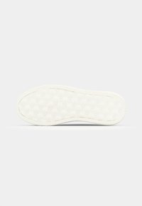 Fehér gumis sneaker talp, amely textúrázott felülettel, ismétlődő logópáterns-szel, lekerekített élekkel és bordázott oldallal rendelkezik, hogy biztosítja a tapadást.