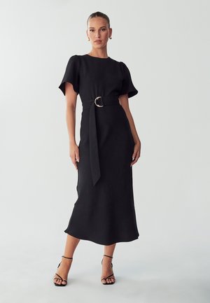 Abito midi nero con maniche corte e voluminose, vita aderente e una larga cintura con fibbia circolare. Texture liscia, silhouette classica.
