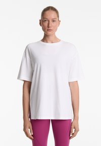 Hvid oversized t-shirt i blød bomuld med rund halsudskæring, korte ærmer og slidser i siderne ved kanten. Simpelt design og glat tekstur.