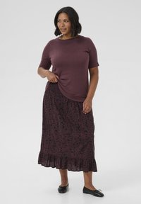 Maroon short-sleeve top paired with a black floral-patterned maxi skirt featuring a ruffled hem and elastic waistband. Black flat shoes.
