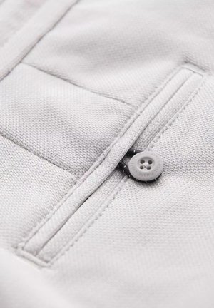 Tissu gris clair avec une surface texturée, présentant une poche zippée et une fermeture à bouton gris rond. Détails de conception simples et fonctionnels.