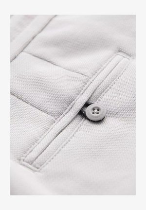 Tissu gris clair avec une surface texturée, présentant une poche zippée et une fermeture à bouton gris rond. Détails de conception simples et fonctionnels.