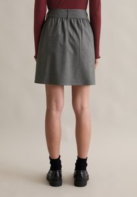 Szürke csíkos szoknya ráncolt derékrésszel, könnyű anyagból készült, fekete cipővel és texturált bokazoknival párosítva.