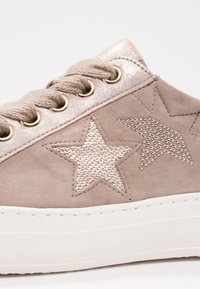 Baskets taupe avec semelle blanche épaisse, lacets scintillants et deux motifs d'étoiles : une en sequins et une cloutée sur le côté.