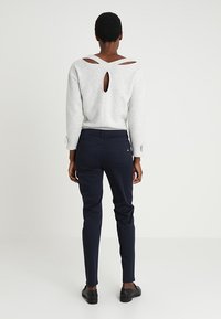 Světle šedý svetr s designem v oblasti zad ve tvaru klíčové dírky a dlouhými rukávy, kombinovaný s tmavě modrými slim-fit kalhotami a černými botami.