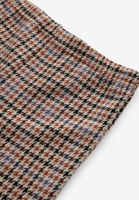 Tissu en tweed avec un motif pied-de-poule en rouille, noir, lavande et beige, montrant une couture piquée et un détail de ceinture.