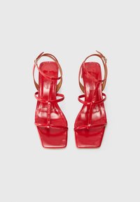 Red patent leather heeled sandals with thin straps, square toes, and an ankle fastening. Smooth texture with a glossy finish.